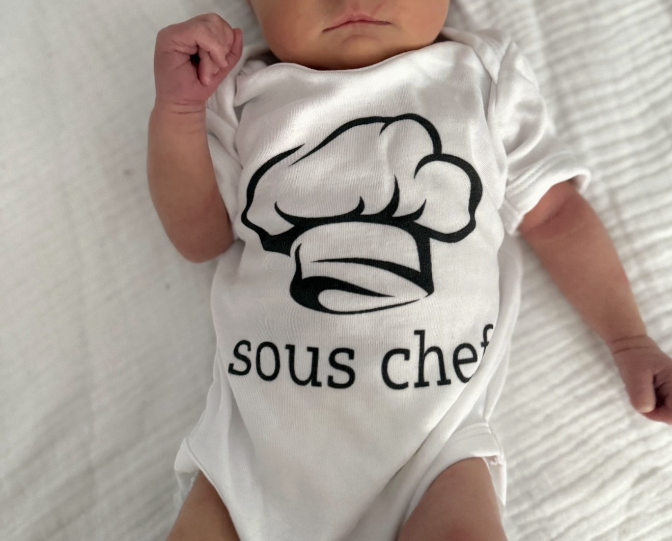 Baby in Strampler mit Aufschrift Sous Chef