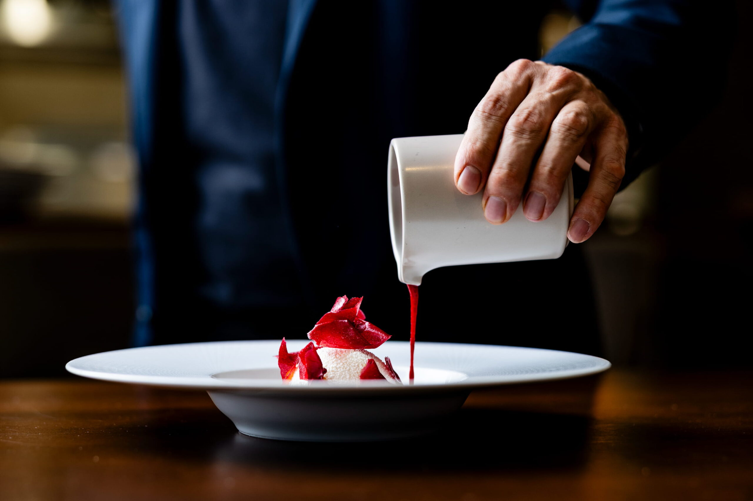 Nachspeise wird angegossen mit Sauce von einer Person im Hintergrund